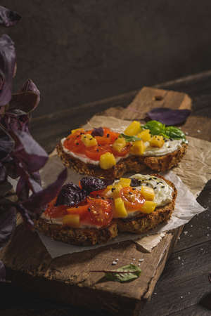 Italian bruschetta with roasted tomatoes, mozzarella cheese, pineapple slices and herbs on a wooden cutting board.の写真素材