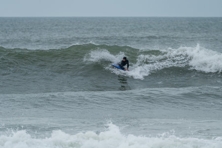 Bodyboarder performing a 360 trick surfing ocean wave on a cloudy winter day.の写真素材