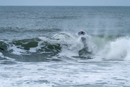 Bodyboarder performing a tube trick surfing ocean wavesurfing ocean wave on a cloudy winter day.