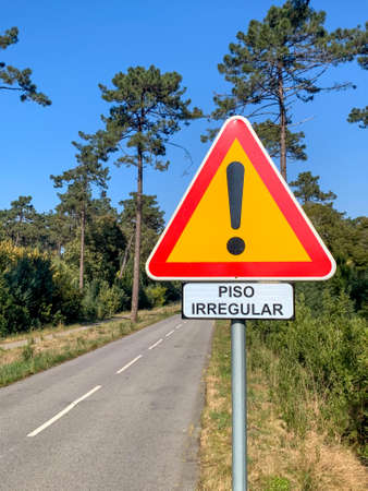 Bumpy road warning sign with an exclamation mark in red triangle on yellow background. Road through forest.の写真素材
