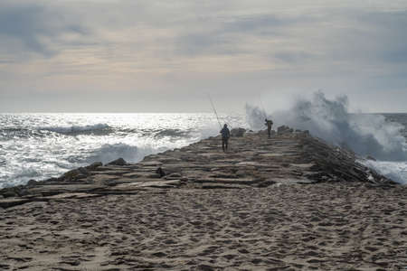 OVAR, PORTUGAL - MAY 18, 2022: Fishermen on the rock wall of Furadouro beach. The advance of the sea...