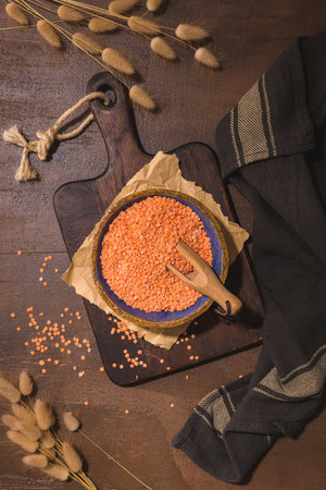 Red lentils in a ceramic bowl with a wooden scoop on a kitchen countertop.の写真素材
