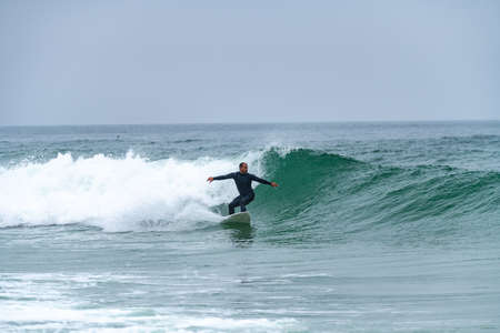 Surfer riding a wave on a foggy morning in Furadouro beach, Ovar - Portugal.