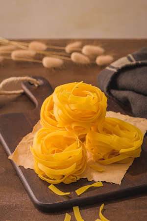 Tagliatelle noodles pasta in wooden cutting board on rustic kitchen countertop.の写真素材