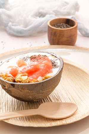 Yogurt with grapefruit, granola, chia and honey served in half a coconut shell on a rose marble kitchen countertop.の写真素材