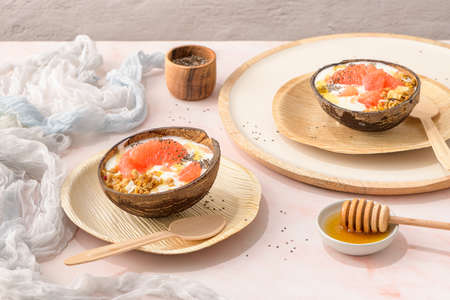 Yogurt with grapefruit, granola, chia and honey served in half a coconut shell on a rose marble kitchen countertop.の写真素材