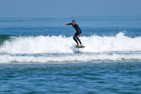 A middle aged man doing some foil surfing or hydrofoil surfing in the sea on a bright sunny day.