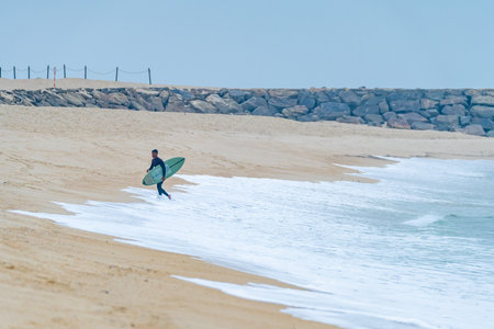 Brazilian surfer leaving the water of the Atlantic coast of Portugal. On a cloudy morning at Furadouro beach, Ovar - Portugal.の写真素材