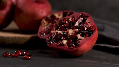 Ripe pomegranate fruit and pomegranate seeds on dark background, close-up. Healthy vegetarian...