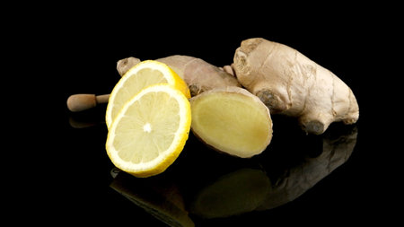 Ginger root drizzler with honey and lemon on black reflective background. Concept of natural ingredients to prevent colds.の写真素材
