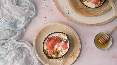 Yogurt with grapefruit, granola, chia and honey served in half a coconut shell on a rose marble kitchen countertop.の写真素材