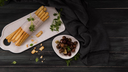 Fresh baked homemade grissini bread sticks in white ceramic tray with olive oil and basil herbs over...