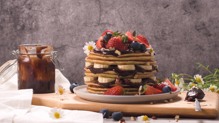 Pancakes with banana, blueberries, strawberries and chocolate sauce on a plate close-up.