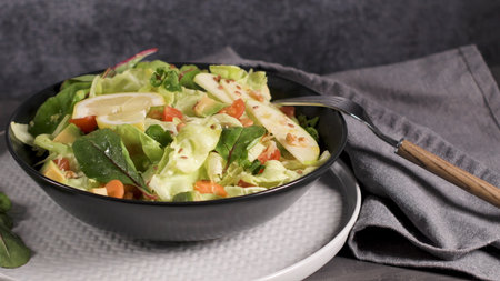 Delicious vegetable salad with apple slices in white ceramic bowl on table.の写真素材