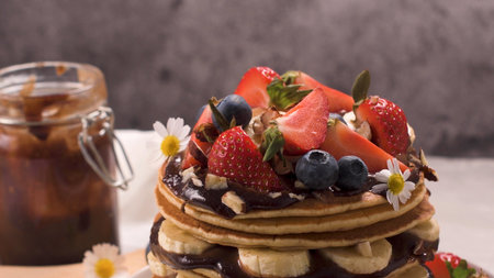 Pancakes with banana, blueberries, strawberries and chocolate sauce on a plate close-up.の写真素材