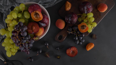 Fruits Still life with fruit on white ceramic bowl. Concrete wall. Dramatic light. Grapes, apricots and plums.の写真素材