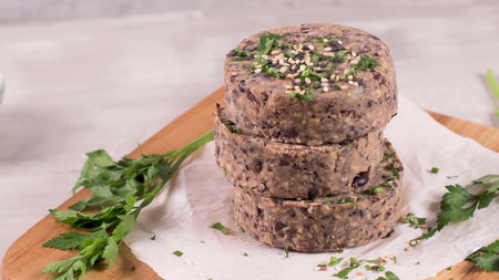 Raw veggie burger with black beans with parsley leaves on wood cutting board.の写真素材