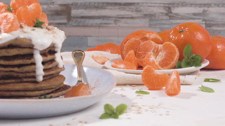 Pancakes with yogurt and tangerines on a light modern kitchen counter top with oat, thyme and mint leaves.の写真素材