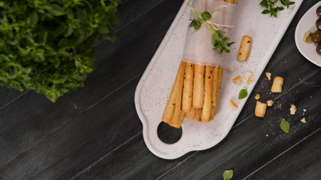 Fresh baked homemade grissini bread sticks in white ceramic tray with olive oil and basil herbs over kitchen counter top.の写真素材