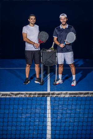 Full length portrait of two sporty young men in sportswear standing on indoor court with paddle rackets in hands after match.の写真素材