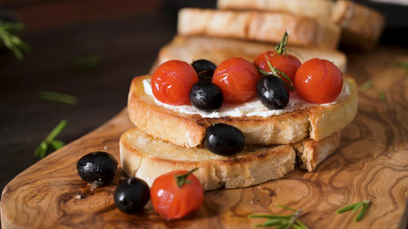 Fresh bruschetta with cream cheese, black olives and cherry tomatoes closeup.