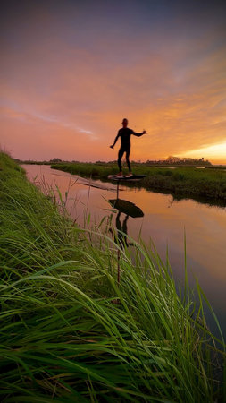 Hydrofoil rider gliding over the water with his board in one of the canals of the Ria de Aveiro in Portugal during sunset.の写真素材