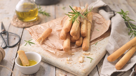 Traditional italian breadsticks grissini with rosemary, olive oil and sesame seeds on wooden...