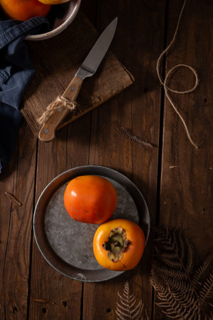 Rustic still life of persimmons on a metal plate with a wooden backdropの写真素材