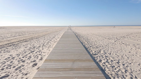 A wooden boardwalk stretches across a vast, sandy beach towards the horizon.の写真素材