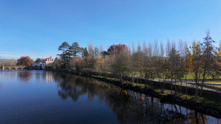 Panoramic view of a river with a stone bridge, a historic building, and a tree-lined path along the...