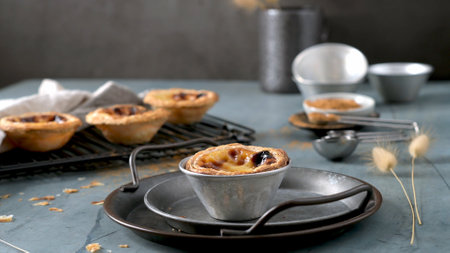 Four Portuguese custard tarts one on a metal tray others on a rack with cinnamon measuring spoons...