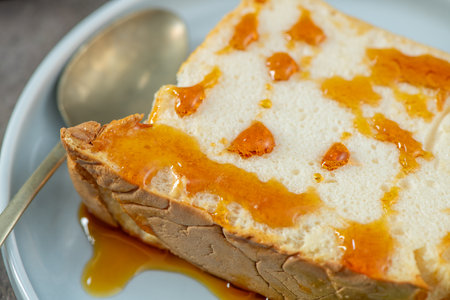 Close-up of a delicious slice of molotof, a traditional caramelized egg white pudding, generously drizzled with sweet syrup on a light blue plate with a silver spoonの写真素材