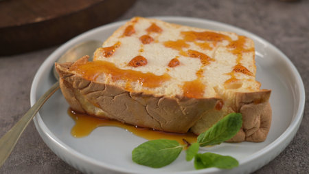 A delectable slice of traditional pudding, generously drizzled with golden caramel sauce and garnished with fresh mint leaves, served on a small round plate with a spoon.の写真素材