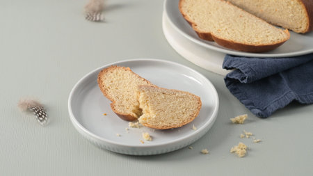 Slices of traditional Portuguese Easter folar on white plates with delicate feathers, hinting at a spring celebration.の写真素材
