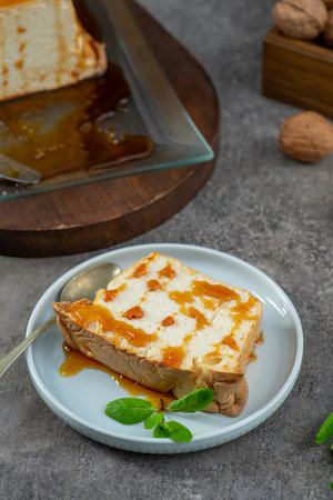 A partially eaten slice of molotof, a traditional caramelized egg white pudding, drizzled with sweet syrup and garnished with mint, sits on a light blue plate with a spoonの写真素材