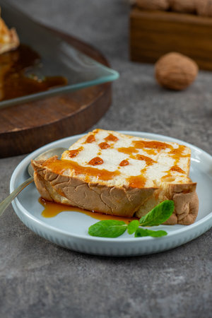 A delightful slice of molotof, a traditional caramelized egg white pudding, drizzled with sweet caramel syrup and garnished with fresh mint leaves, rests on a light blue plate with a spoonの写真素材