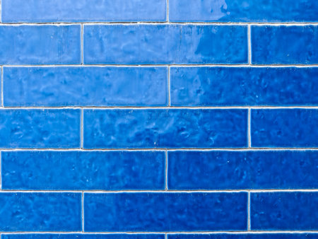A close-up of a wall featuring various shades of blue rectangular tiles, creating a textured and gradient effect across the surface.の写真素材