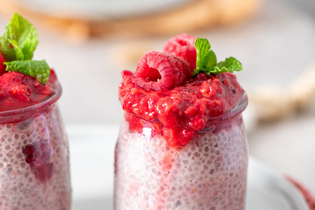A macro close-up of two glass jars of homemade chia seed pudding, topped with a generous layer of...
