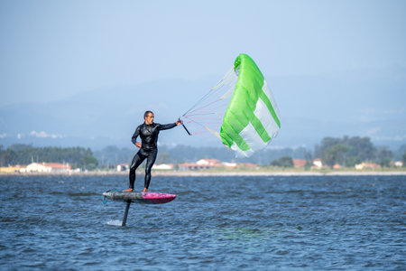 A middle-aged man in a wetsuit glides on a hydrofoil board with a green and white kite, looking at...
