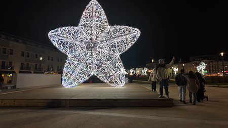 AVEIRO, PORTUGAL - DECEMBER 1, 2025: A large, white, intricate LED star sculpture, part of Aveiro's Christmas display, is captured on a wooden platform on a city plaza at night, with several people taking photos of it.のeditorial素材