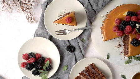 A decadent chocolate layer cake topped with smooth salted caramel and a pile of fresh raspberries and blackberries. The scene is shot from a top-down perspective on a bright marble surface.の写真素材