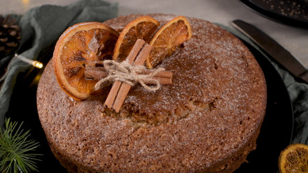 Christmas orange cake decorated with dried oranges on Christmas decorated kitchen countertop.
