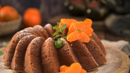 A golden-brown citrus bundt cake topped with juicy mandarin segments and mint leaves. The rustic...