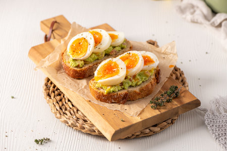 Two slices of toasted sourdough topped with mashed avocado and jammy soft boiled eggs. High angle...