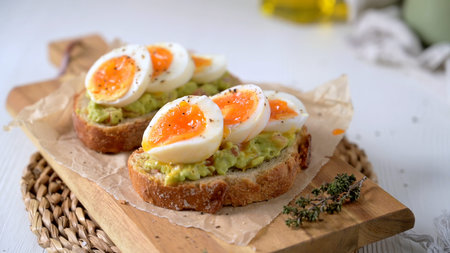 Two slices of crusty sourdough bread topped with creamy guacamole and jammy soft boiled egg halves....