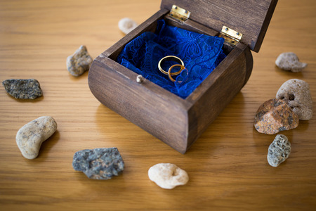 Wedding golden rings inside the open wooden box with stones around. Ceremony