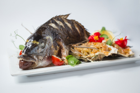 Backed dorada with salsa in shell, green, tomatoes, red flowers and lemon.の写真素材