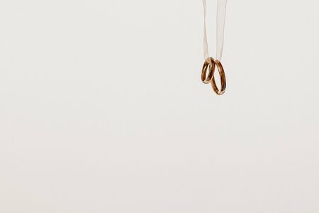 Two golden wedding rings hanging on a ribbon, isolated on white background.の写真素材