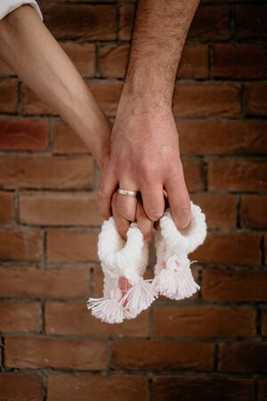 Young couple are waiting for baby are holding little white socks in front of red bricks.の写真素材