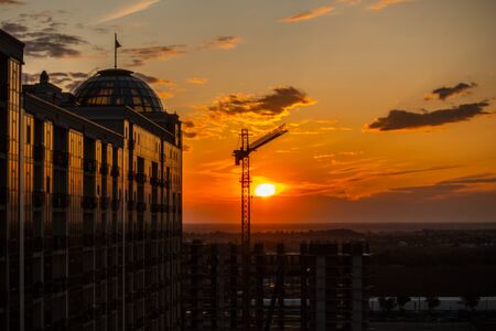 Dark Silhouette of construction crane and building from glass on sunset sky background. Used for lifting equipment in the construction of high-rise buildings behind the sky. Odesa, Ukraine. Kadorr.の写真素材